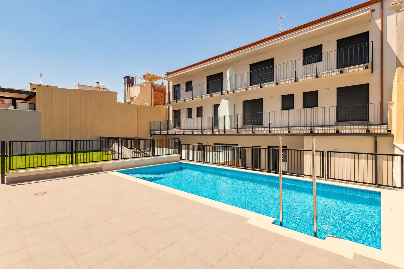 Piscina comunitaria con solárium y césped, junto a las terrazas de las viviendas